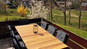 Un patio al aire libre con una mesa de madera y sillas negras, rodeado por un bajo muro de ladrillo y vistas a casas y árboles.