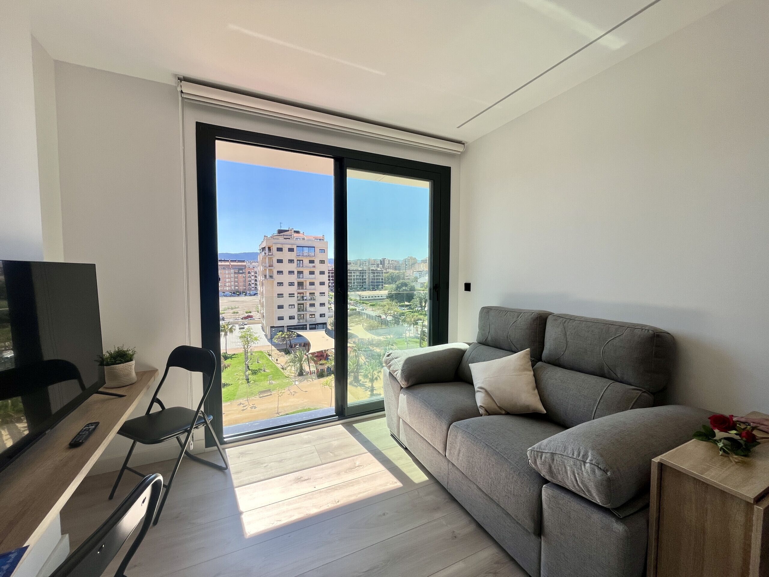 Een moderne woonkamer met een grijze bank, een televisie en een eethoek met een stoel en tafel.