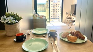 Et spisebord med tallerkener, bestik og en croissant med udsigt over byen.