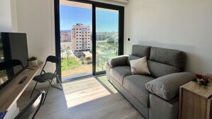Een moderne woonkamer met een grijze bank, een televisie en een eethoek met een stoel en tafel.