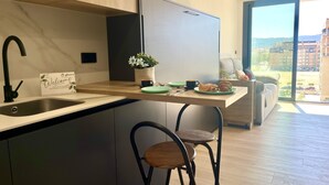 Een moderne keuken met een ingebouwde spoelbak, een koelkast, een eethoek met tafel en stoelen, en uitzicht op de stad door grote ramen.