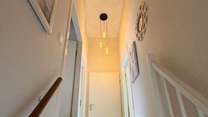 Un escalier étroit avec une rampe en bois, un luminaire et une porte en haut.