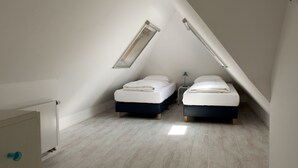 Une petite pièce avec un toit en pente, comprenant deux lits, une table de chevet et une lampe.