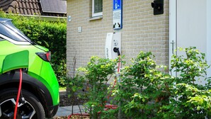 Une voiture verte est garée à côté d’un bâtiment où se trouve un panneau indiquant un espace de stationnement et une borne de recharge pour véhicules électriques.