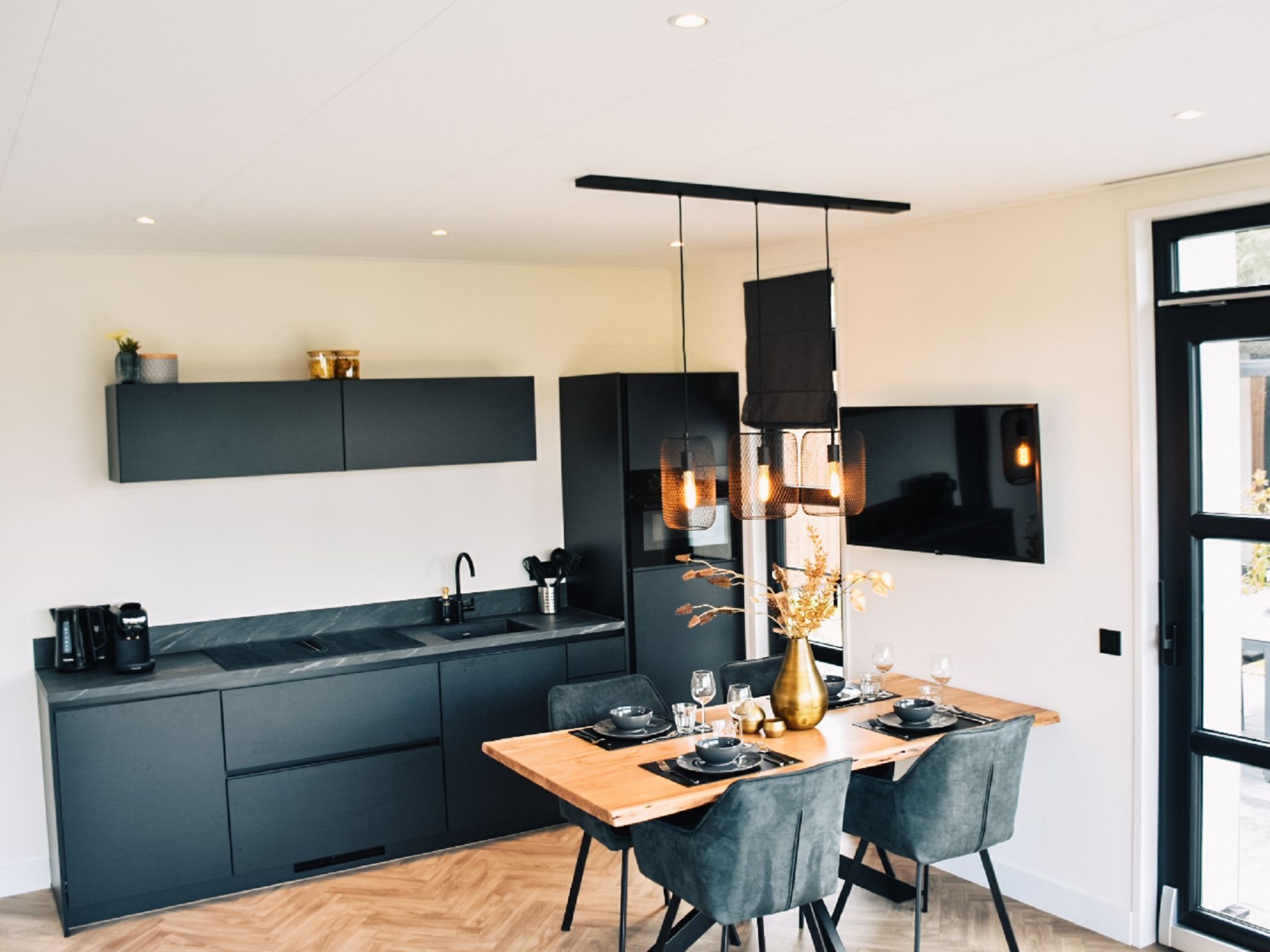 Een moderne keuken met donkere kastjes, een houten eettafel en een hanglamp.