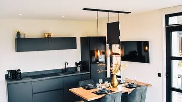 Een moderne keuken met donkere kastjes, een houten eettafel en een hanglamp.
