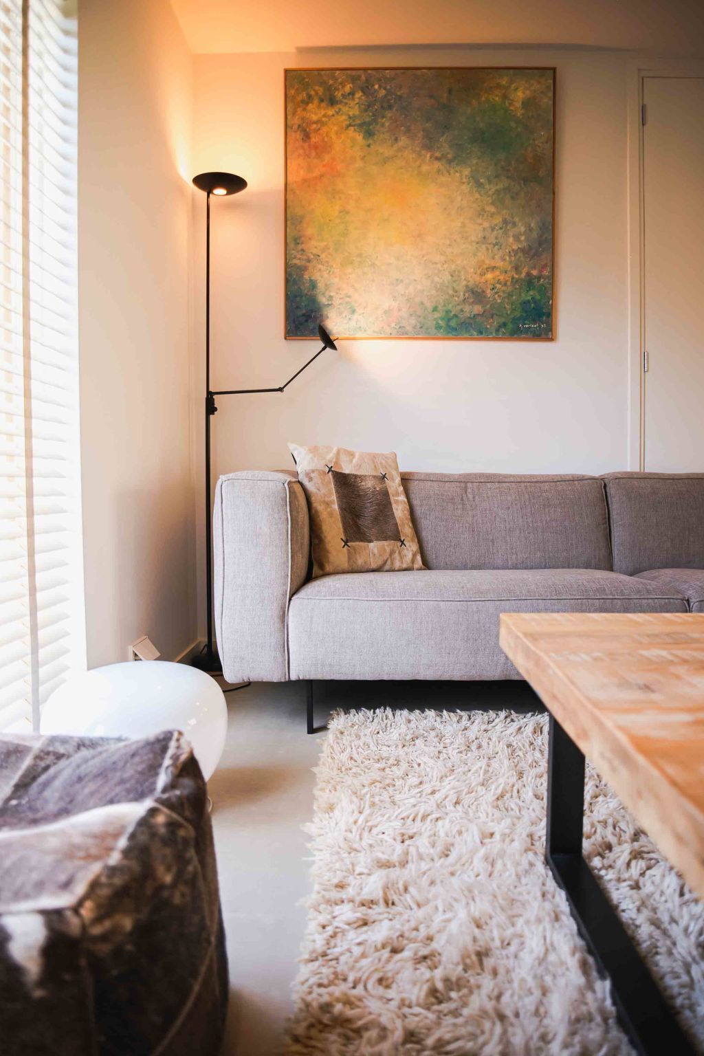 Una sala de estar con un sofá gris, un felpudo blanco, una mesa de centro de madera y un cuadro en la pared.