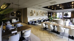 Un restaurante moderno con varias zonas de comedor, que incluyen un bar y un espacio con mesas y sillas redondas.