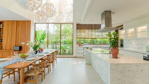 A modern kitchen with a large island, wooden dining table, and chairs. - 5BRs villas for a perfect family getaway (Da Nang)