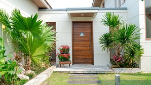 A modern house with a wooden front door, a small porch, and a garden with tropical plants. - 5BRs villas for a perfect family getaway (Da Nang)