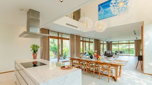 A modern kitchen with a marble island, large windows, and a dining area with wooden furniture. - 5BRs villas for a perfect family getaway (Da Nang)