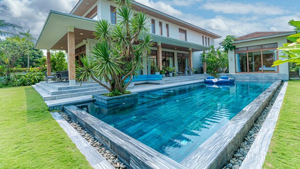 A modern house with a swimming pool, a covered patio, and lush greenery. - 5BRs villas for a perfect family getaway (Da Nang)