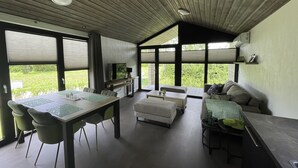 A modern interior with a dining area, sofa, and large windows offering a view of greenery. - De Parel by Interhome (Scherpenisse)