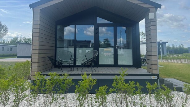 A modern outdoor structure with a glass entrance, two chairs, and a small deck. - De Parel by Interhome (Scherpenisse)