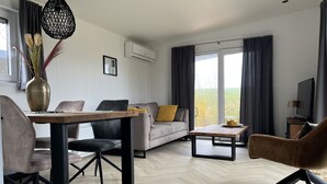 Een moderne woonkamer met een bank, salontafel en stoelen. Er is een eettafel met stoelen, een hanglamp en een televisie.