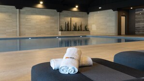 A modern indoor pool area with a clear view of the pool, a towel on a bench, and a cactus wall.