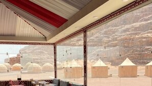 An indoor seating area with patterned floor tiles, a long table, and cushioned benches. - Bedouin life (Wadi Rum)