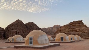 A row of dome-shaped tents with doors and windows, set against a desert landscape with rocky formations. - Bedouin life (Wadi Rum)