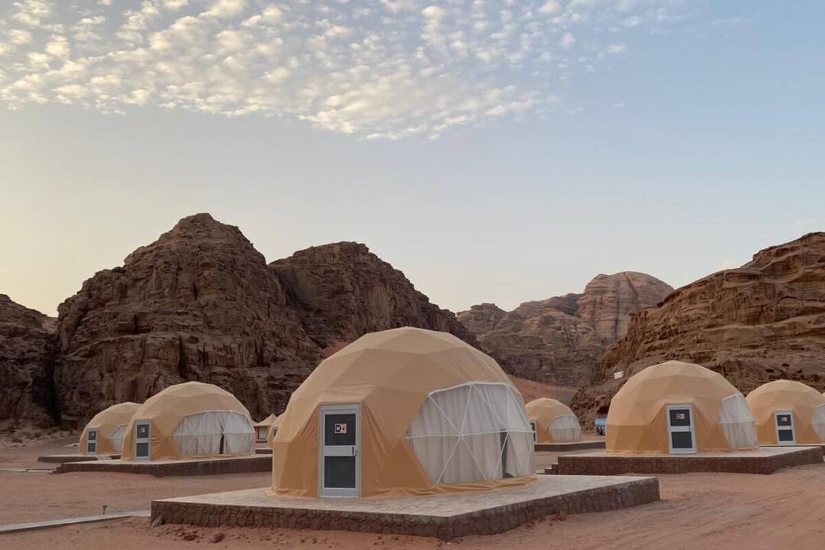 A row of dome-shaped tents with doors and windows, set against a desert landscape with rocky formations.