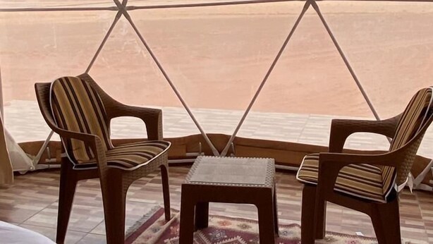 A room with a large window, two chairs, a small table, and a bed. - Bedouin life (Wadi Rum)