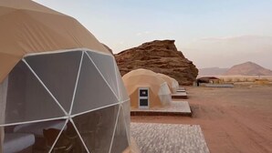 A desert landscape with a large geodesic dome tent and a smaller structure with a flat roof. - Bedouin life (Wadi Rum)