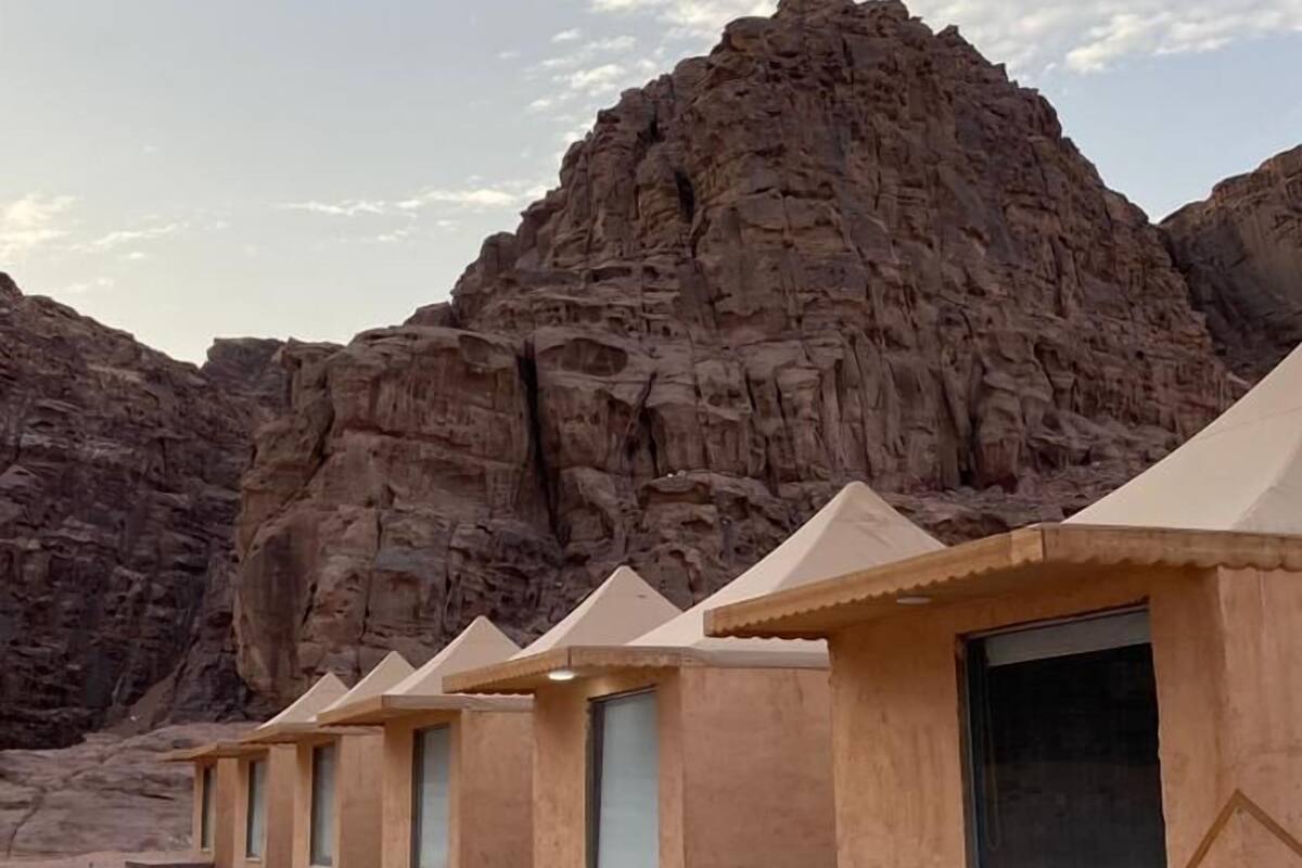 A row of beige-roofed, single-story buildings with windows, set against a rocky desert backdrop.