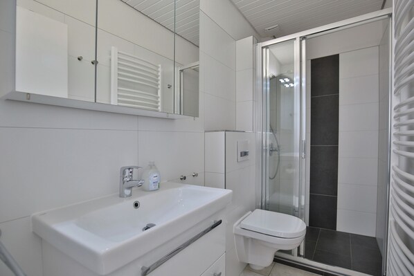 A modern bathroom with a white sink, toilet, and glass shower enclosure. - Die Insel Appartement 19 (Timmendorfer Strand)