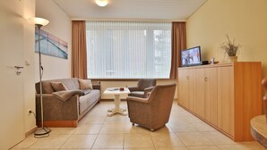 A living room with a sofa, armchair, coffee table, TV, and a cabinet. - Die Insel Appartement 19 (Timmendorfer Strand)