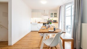 A modern kitchen with white cabinets, a wooden countertop, and a dining area with a wooden table and white chairs. - Sonnig. Terrasse. Zentral (Westerland)
