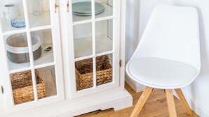 A white cabinet with glass doors containing baskets and a bowl, next to a white chair. - Sonnig. Terrasse. Zentral (Westerland)