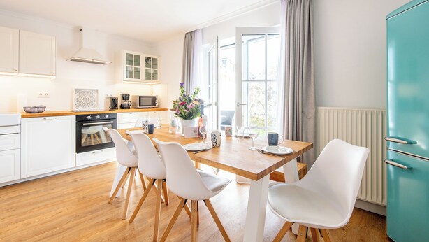 A modern kitchen with white cabinets, a wooden countertop, and a dining area with white chairs. - Sonnig. Terrasse. Zentral (Westerland)