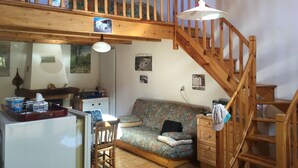 Una habitación acogedora con una escalera de madera, un sofá, una mesa de comedor y un refrigerador.