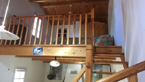 Una escalera de madera con barandilla que lleva a un dormitorio en un altillo.
