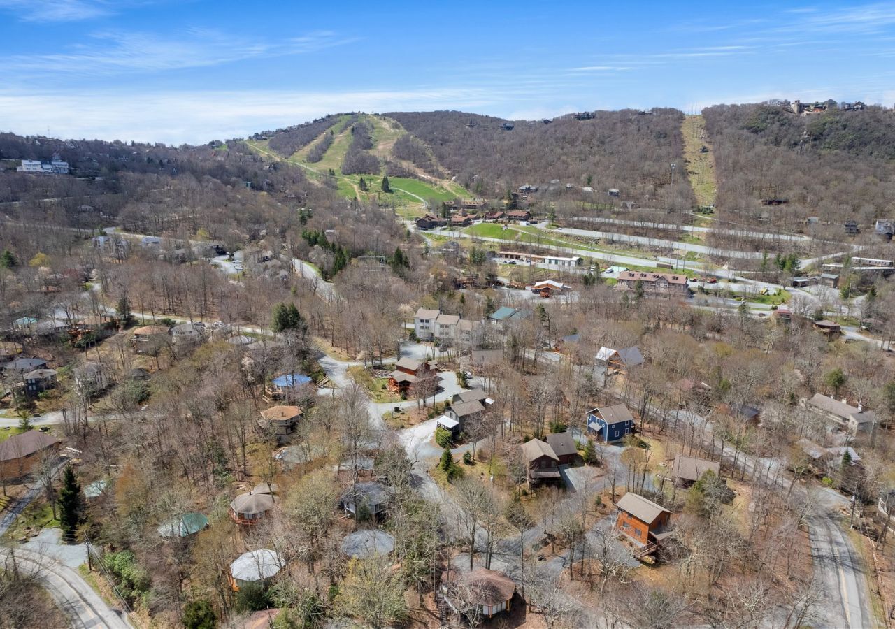 Vue aérienne d’un quartier résidentiel avec des maisons, des routes et un paysage vallonné en arrière-plan.
