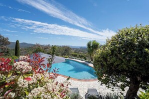 A swimming pool with a stone deck, surrounded by lush greenery and a view of distant hills.