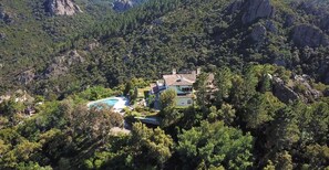 A villa surrounded by dense forest, with a swimming pool and a mountain backdrop.