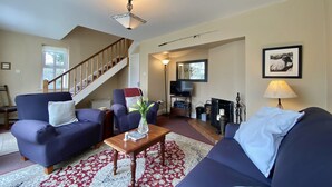 Un salon avec deux canapés, une table basse, un téléviseur, une cheminée et un escalier.
