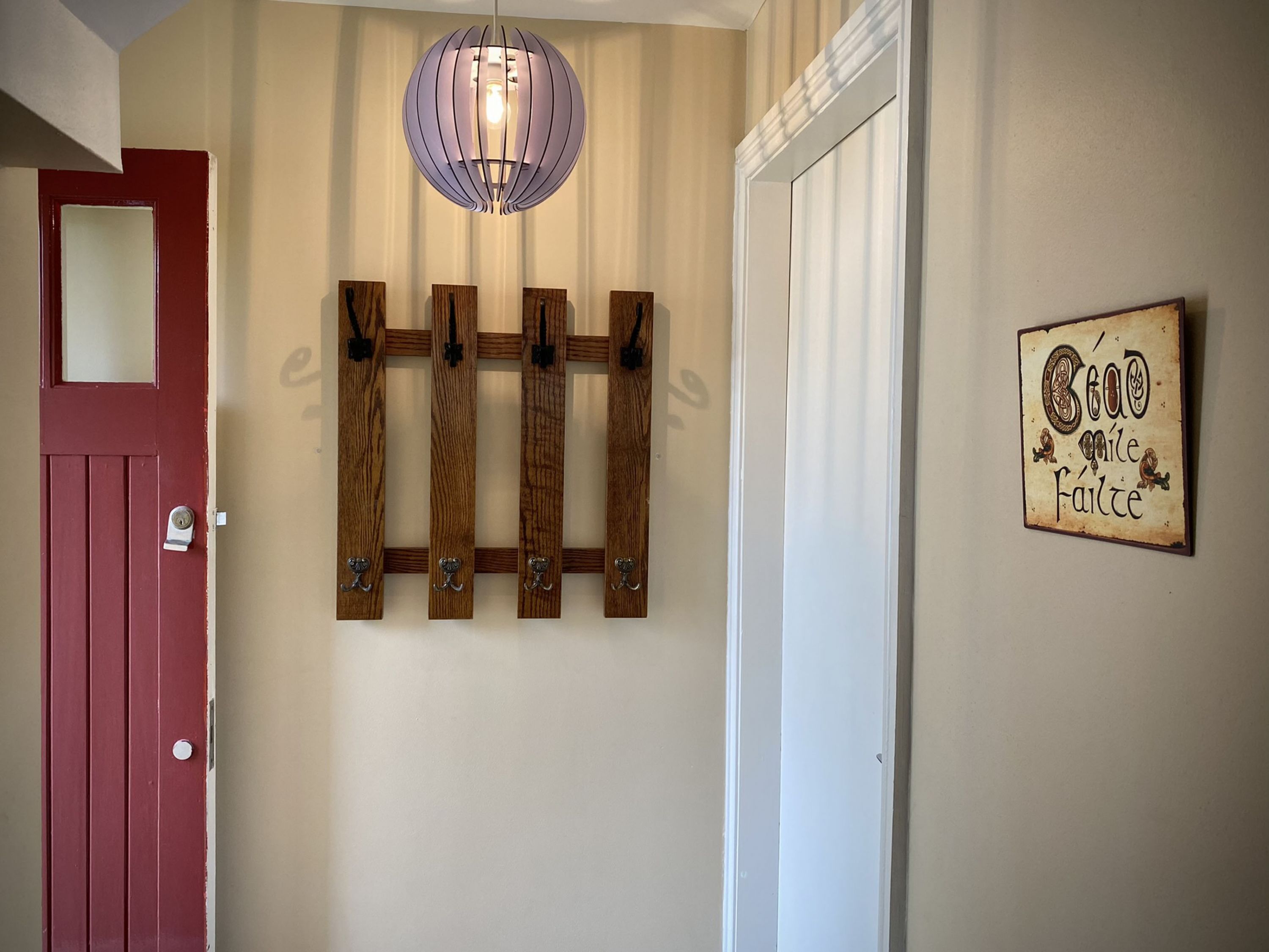 Un pasillo con una puerta roja, un perchero de madera, una lámpara colgante y un cartel en la pared.