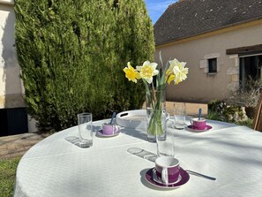 An outdoor table set with a vase of daffodils, a teapot, cups, and glasses.