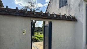 A doorway leading to a courtyard with a tiled floor, a metal gate, and a tree in the background. - All-inclusive cottage between Moulins and Saint-Pourçain-sur-Sioule (Contigny)