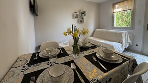 A dining area with a table set for four, a sofa, a window with blinds, and a wall-mounted TV. - All-inclusive cottage between Moulins and Saint-Pourçain-sur-Sioule (Contigny)