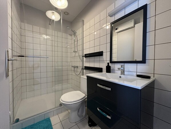 Une salle de bain moderne avec une douche à parois de verre, des toilettes blanches, un meuble-lavabo noir avec un miroir et un lavabo blanc.