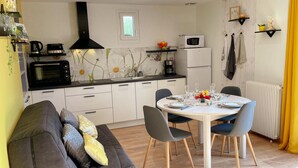 A modern kitchen with white cabinets, a black stove, and a microwave. There is a dining table with chairs and a sofa with cushions. - Charming Gîte with Private Garden, Close to Amboise, Perfect for Relaxation and Exploration (Pocé-sur-Cisse)