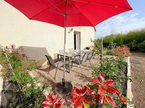An outdoor patio with a table and chairs, a red umbrella, and potted plants. - Charming Gîte with Private Garden, Close to Amboise, Perfect for Relaxation and Exploration (Pocé-sur-Cisse)
