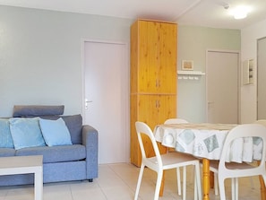 Un espace de vie compact comprenant un canapé, une table à manger, des chaises et une armoire en bois.