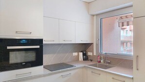 A modern kitchen with a built-in oven, a coffee maker, and a window with a view of buildings. - Air-Conditioned T2 with Parking, Bormes-les-Mimosas (Bormes-les-Mimosas)