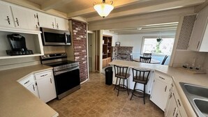 Una cocina con armarios blancos, una pared de ladrillo decorativa, un microondas integrado, una cafetera y un comedor con dos sillas.