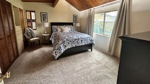Un dormitorio con cama, una silla, una mesita y un aparador.