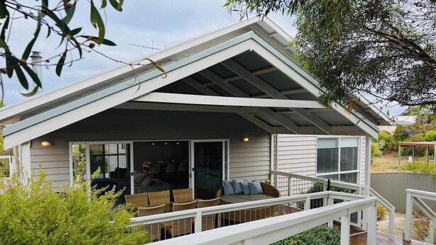 Une maison moderne dotée d’un patio couvert, d’une terrasse et d’une grande fenêtre donnant sur un jardin.