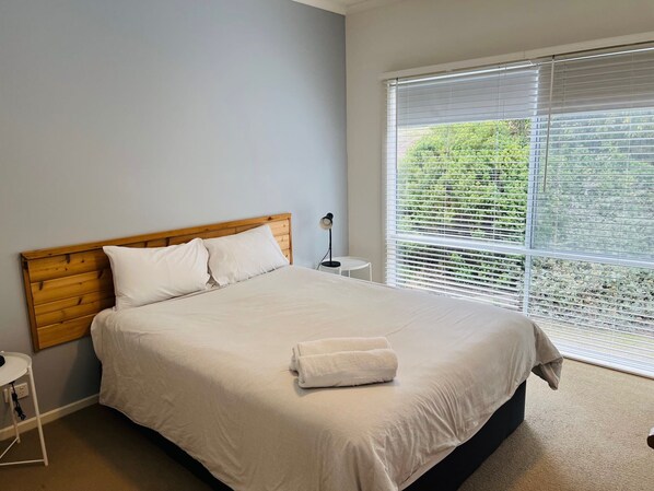 A neatly made bed with white linens, a wooden headboard, and a bedside table with a lamp.